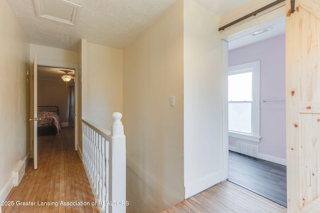hallway with visible vents, attic access, an upstairs landing, and hardwood / wood-style flooring