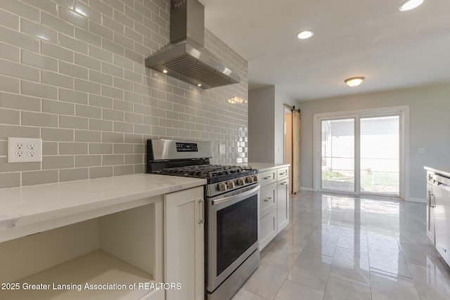 kitchen featuring wall chimney range hood, a barn door, stainless steel gas range oven, baseboards, and backsplash