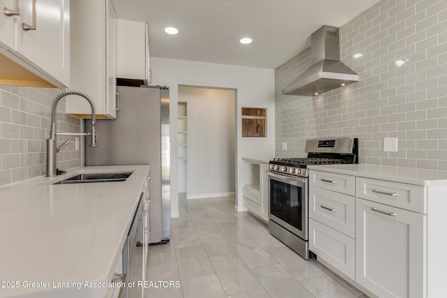 kitchen featuring wall chimney range hood, appliances with stainless steel finishes, a sink, and tasteful backsplash