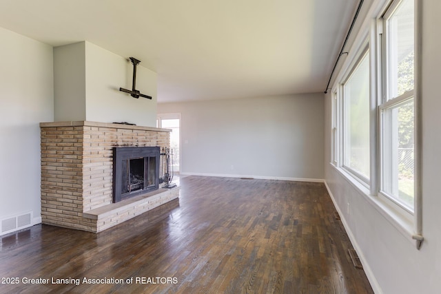 unfurnished living room featuring visible vents, dark wood-style flooring, a brick fireplace, and baseboards