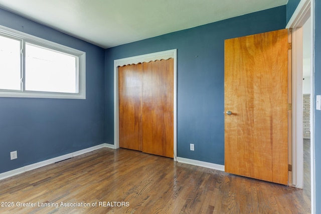 unfurnished bedroom with baseboards, wood finished floors, and a closet