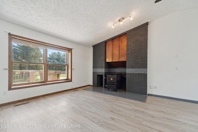 1971 N Michigan Rd, Eaton Rapids, MI 48827 - unfurnished living room featuring light wood-style flooring, a textured ceiling, vaulted ceiling, and a wood stove