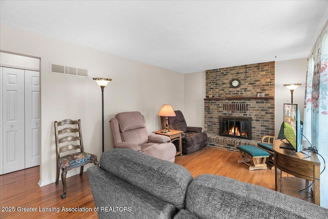 living room featuring a brick fireplace, wood finished floors, and visible vents