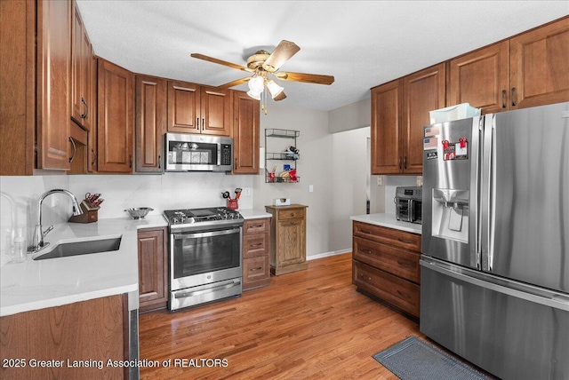 kitchen featuring brown cabinetry, a ceiling fan, light wood-type flooring, a sink, and stainless steel appliances