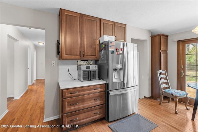 kitchen with stainless steel refrigerator with ice dispenser, light countertops, light wood-style flooring, and brown cabinets