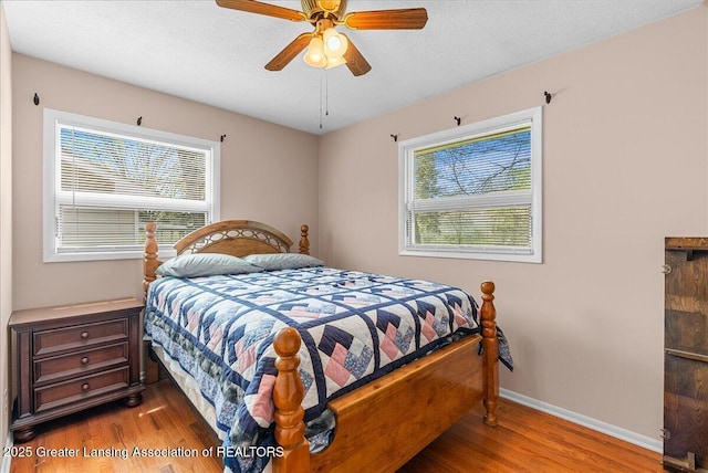 bedroom with a ceiling fan, baseboards, multiple windows, and wood finished floors