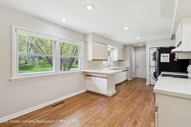 4793 Ottawa Dr, Okemos, MI 48864 - kitchen featuring stacked washing machine and dryer, light wood finished floors, white cabinets, range, and light countertops