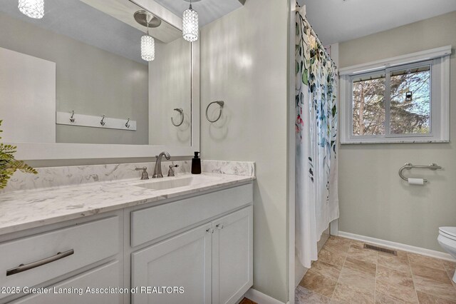 bathroom featuring vanity, toilet, stone finish floor, baseboards, and visible vents