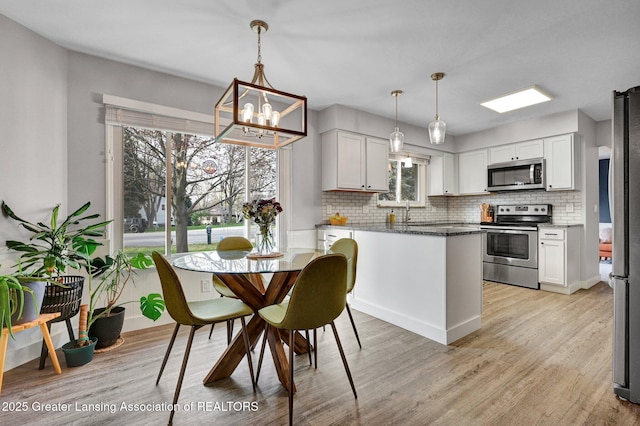 kitchen with tasteful backsplash, light wood-type flooring, a chandelier, stainless steel appliances, and white cabinetry