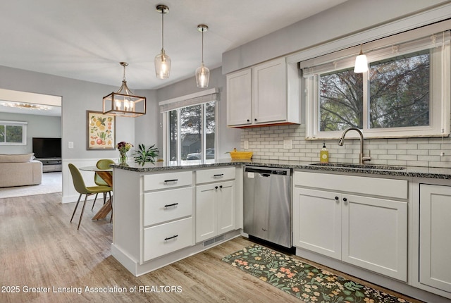 kitchen with a peninsula, tasteful backsplash, a sink, light wood-style flooring, and dishwasher