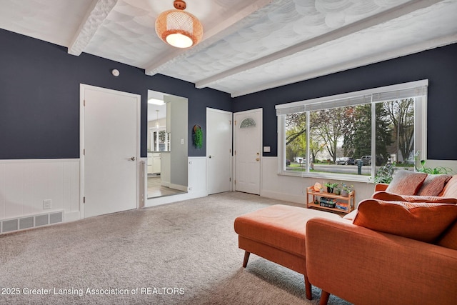 living area featuring wainscoting, beamed ceiling, visible vents, and light carpet