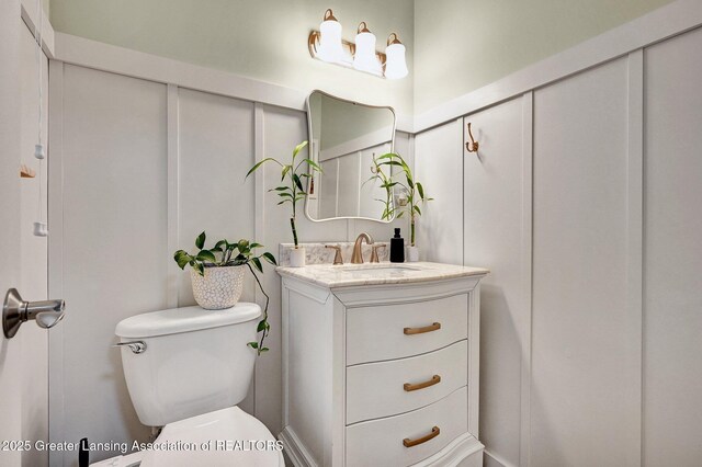 half bath with vanity, a decorative wall, and toilet