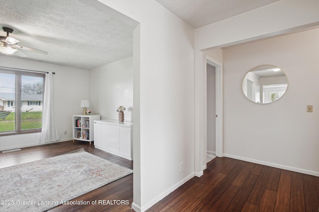 hallway with a textured ceiling, baseboards, and dark wood finished floors