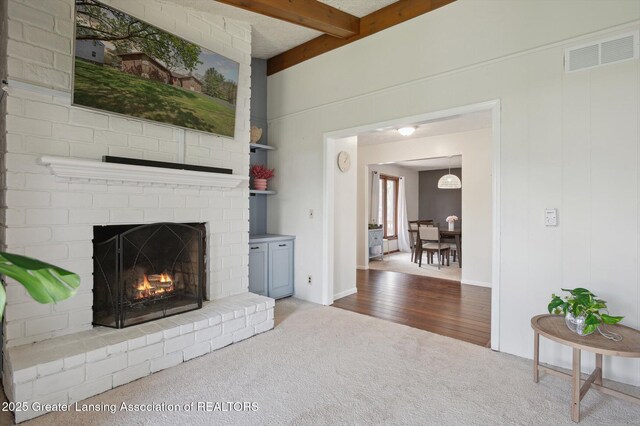 carpeted living area with beamed ceiling, visible vents, and a fireplace