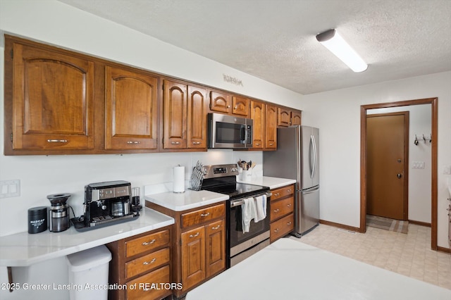 kitchen featuring light countertops, a textured ceiling, brown cabinetry, stainless steel appliances, and light floors