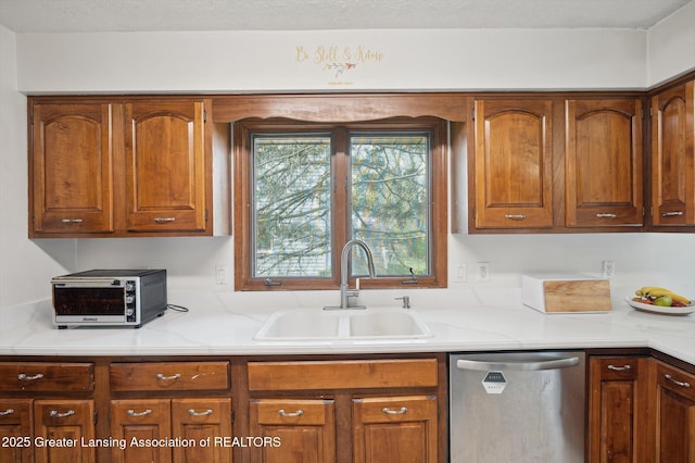 kitchen featuring stainless steel dishwasher, a toaster, light countertops, brown cabinets, and a sink