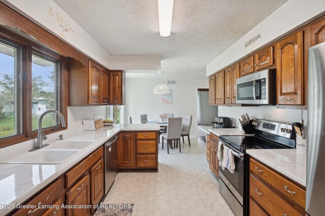 kitchen featuring brown cabinetry, light floors, a textured ceiling, a sink, and stainless steel appliances