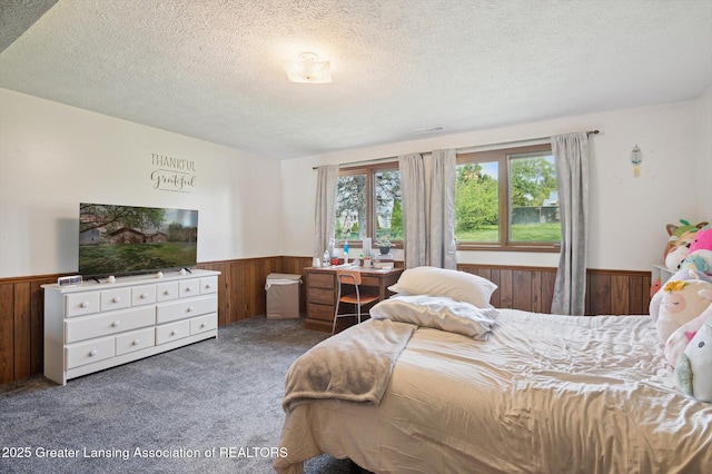bedroom featuring a textured ceiling, visible vents, wainscoting, wooden walls, and carpet flooring