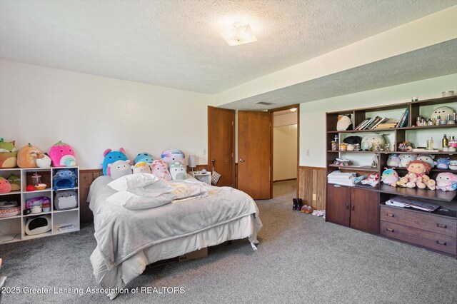 carpeted bedroom with a textured ceiling and a wainscoted wall
