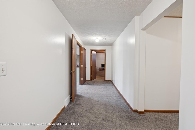 hallway with baseboards, carpet, a textured ceiling, and visible vents