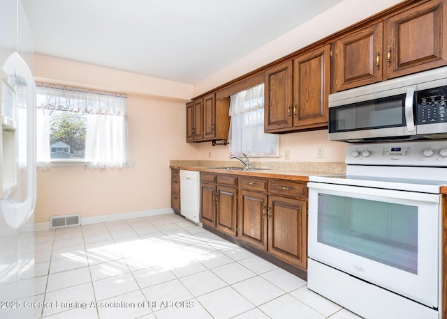 kitchen featuring visible vents, white appliances, light countertops, a sink, and a wealth of natural light