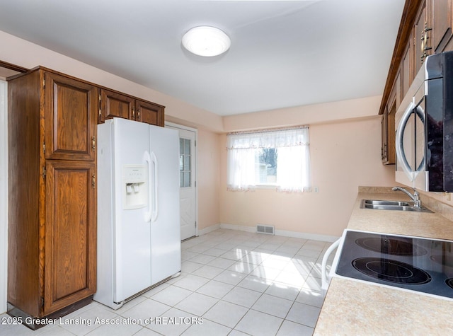 kitchen featuring visible vents, a sink, stainless steel microwave, white fridge with ice dispenser, and light tile patterned flooring