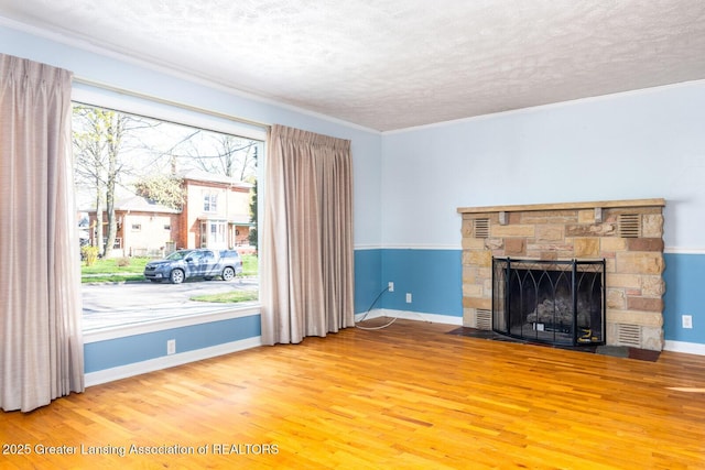 unfurnished living room featuring crown molding, wood finished floors, a fireplace, baseboards, and a textured ceiling