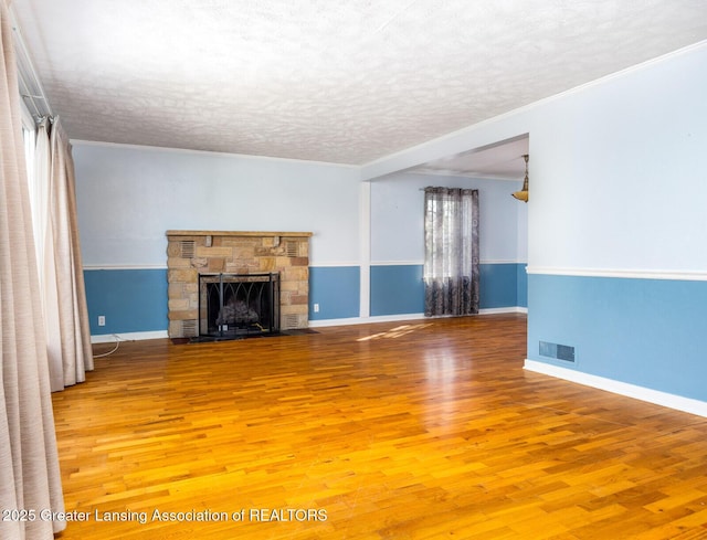 unfurnished living room with a textured ceiling, visible vents, a stone fireplace, and wood finished floors