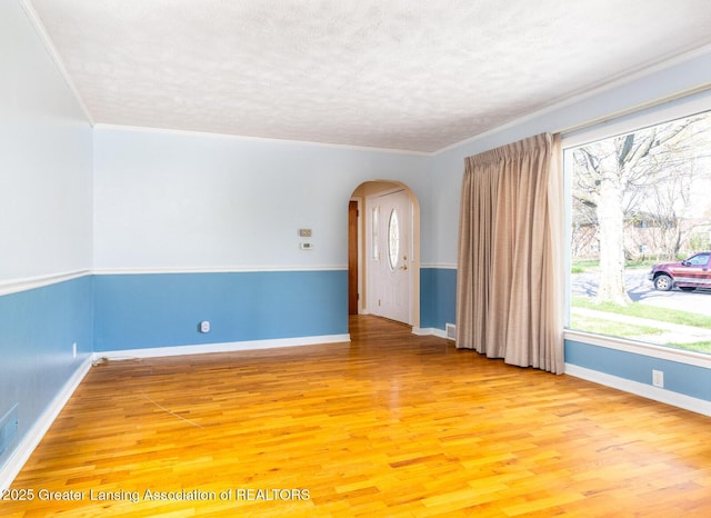 unfurnished room with light wood-style floors, arched walkways, a textured ceiling, and a wealth of natural light