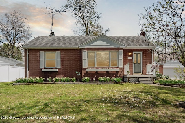 view of front facade featuring brick siding, fence, a chimney, and a front lawn