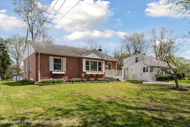 view of front facade with a shingled roof, brick siding, a deck, a front yard, and a chimney