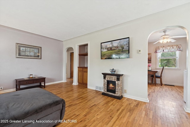 living area featuring ceiling fan, light wood-style floors, arched walkways, baseboards, and visible vents