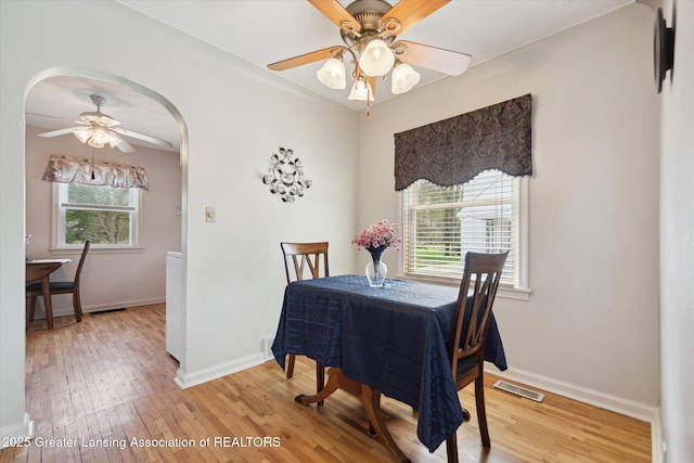 dining space featuring baseboards, arched walkways, ceiling fan, and light wood-style flooring