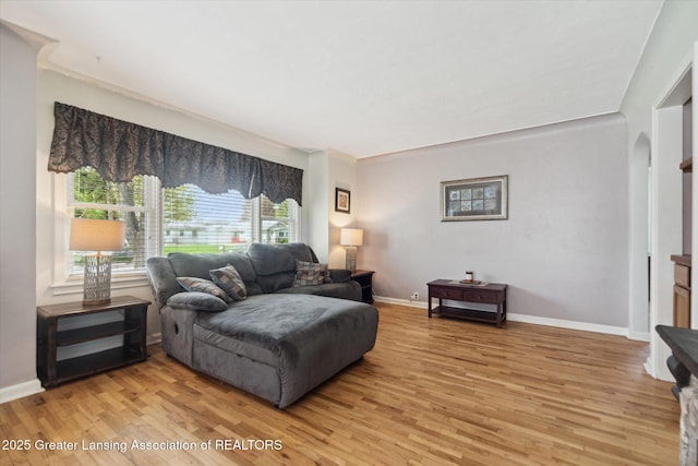 living area featuring arched walkways, baseboards, and light wood finished floors
