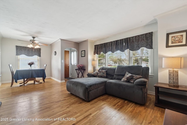 living room featuring baseboards, arched walkways, light wood finished floors, and ceiling fan