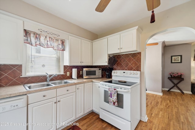 kitchen featuring a sink, white appliances, arched walkways, a ceiling fan, and white cabinetry