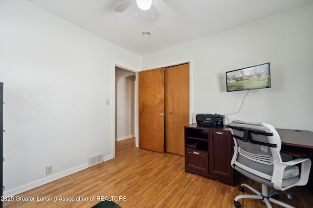 home office with visible vents, light wood-style floors, baseboards, ceiling fan, and arched walkways