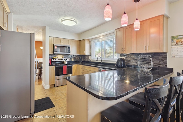 kitchen with dark countertops, appliances with stainless steel finishes, a sink, a peninsula, and tasteful backsplash