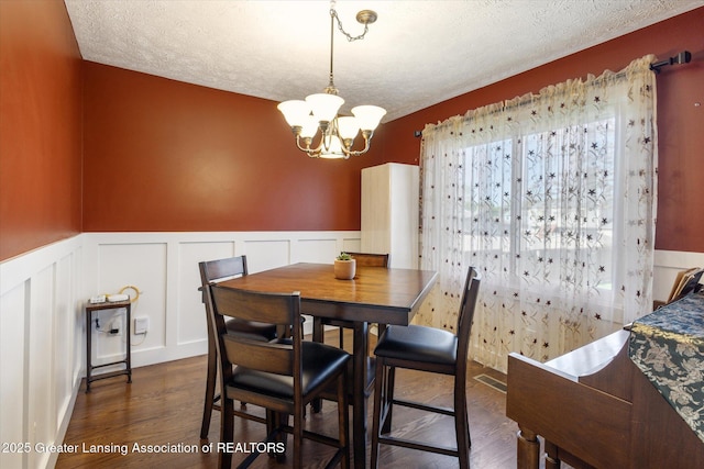 dining area with a wainscoted wall, a decorative wall, dark wood-style floors, and a chandelier