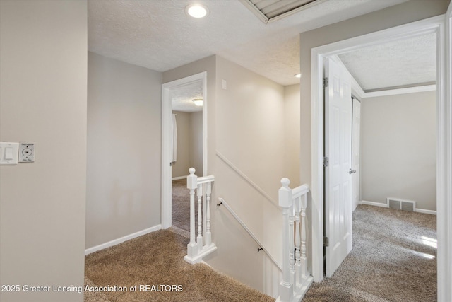 hall featuring carpet flooring, a textured ceiling, baseboards, an upstairs landing, and visible vents