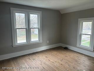 512 S Cedar St, Owosso, MI 48867 - empty room featuring baseboards, a wealth of natural light, lofted ceiling, and wood finished floors
