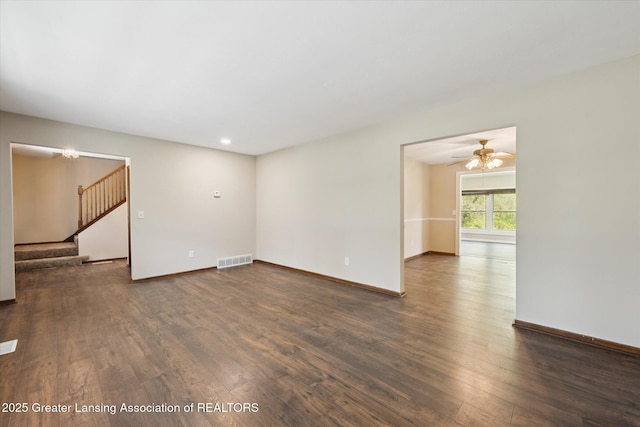 unfurnished living room with dark wood-style flooring, baseboards, visible vents, and stairway