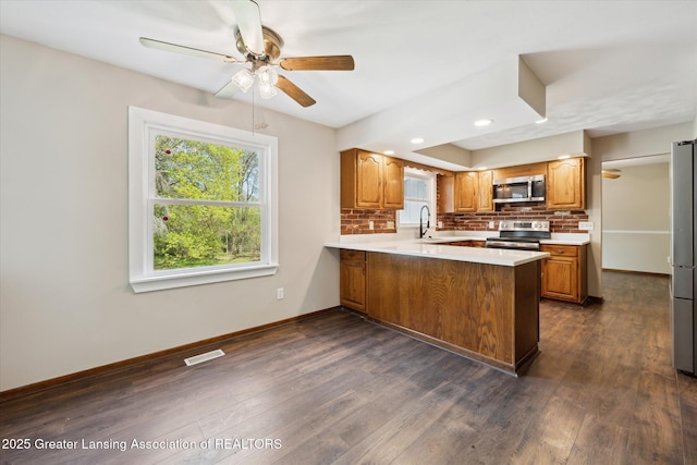 kitchen featuring decorative backsplash, a ceiling fan, a sink, a peninsula, and stainless steel appliances