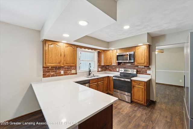 kitchen featuring decorative backsplash, a sink, light countertops, a peninsula, and stainless steel appliances