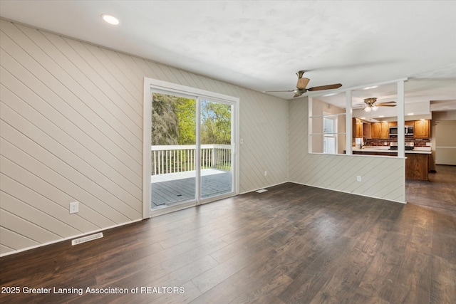 unfurnished living room featuring visible vents, wood walls, ceiling fan, recessed lighting, and dark wood finished floors