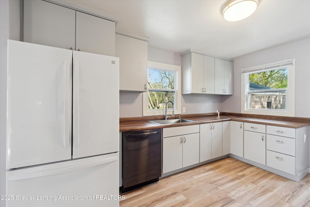 kitchen featuring a sink, freestanding refrigerator, light wood finished floors, dishwashing machine, and a wealth of natural light