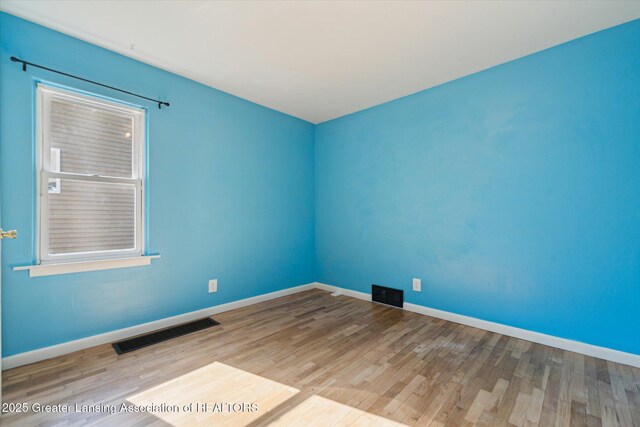 empty room featuring baseboards, visible vents, and wood finished floors