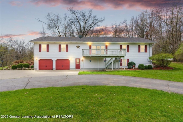 raised ranch featuring stairs, an attached garage, a wooden deck, a front yard, and driveway