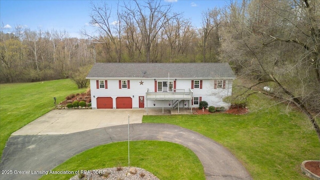 raised ranch with a view of trees, driveway, a front lawn, and a garage