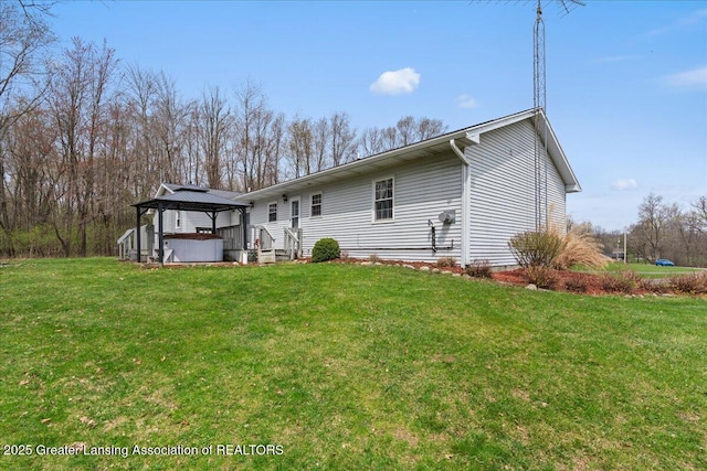 rear view of house featuring a gazebo, a jacuzzi, and a lawn